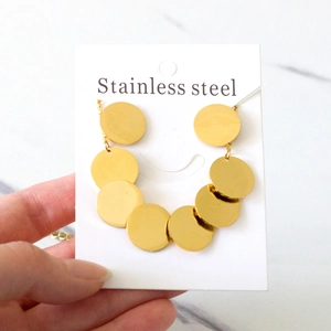 Détail de pendentifs disques dorés superposés sur un collier en acier inoxydable épuré