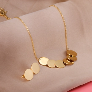 Détail d'un ensemble collier et boucles d'oreilles en acier doré sur soie beige