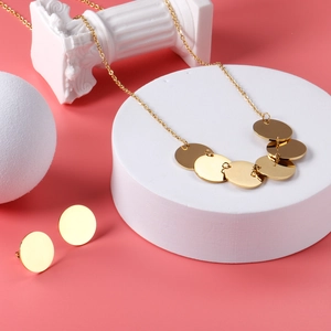 Gros plan d'un ensemble collier et boucles d'oreilles disque doré sur fond rose poudré