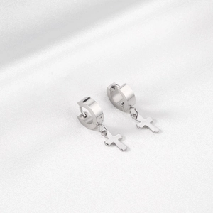 Détail macro de boucles d'oreilles créoles en acier argenté avec pendentif croix sur soie blanche
