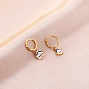 Détail de boucles d'oreilles planète dorées avec breloques en émail sur fond de soie élégant