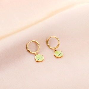 Gros plan de boucles d'oreilles planète dorées avec émail vert sur tissu de soie rose