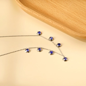 Dettaglio collana d'argento con sette ciondoli a fiore blu su sfondo beige morbido