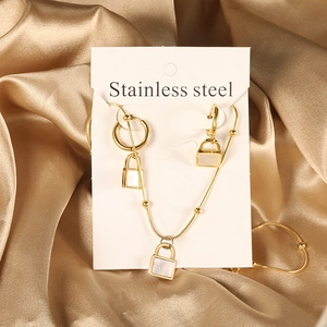 Macro detail of gold stainless steel padlock necklace and stud earrings set with white inlay