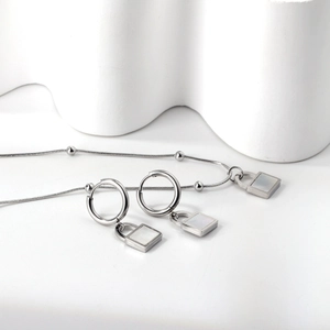 Detail of square shell pendant necklace and hoop earrings on minimalist background