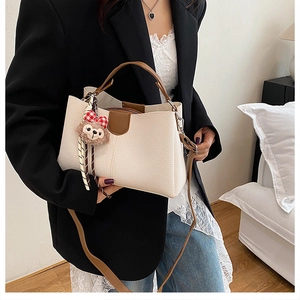Détail du sac seau beige à motif litchi avec poignée marron et breloque en peluche