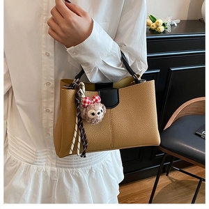 Détail d'un sac seau en cuir grainé avec un pendentif ours en peluche et poignée noire