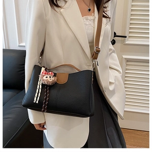 Détail du sac seau en cuir grainé noir avec poignées marron et pendentif en peluche