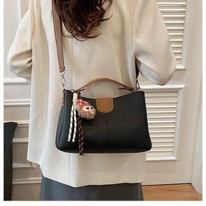 Détail du sac fourre-tout en cuir noir avec bandoulière marron et charm de singe en peluche