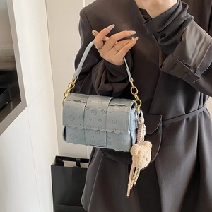 Petit sac tissé bleu clair avec pendentif ours porté sur un blazer noir chic