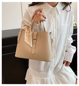 Détail du sac seau beige texturé avec un foulard en soie enroulé sur l'anse