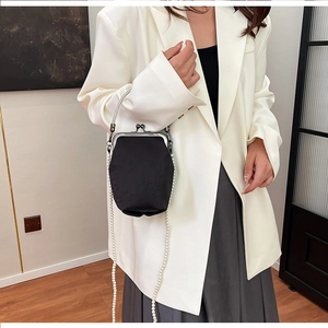 Détail du sac à fermoir en brocart noir avec motifs floraux et chaîne de perles élégante