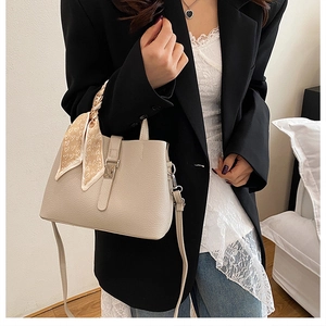 Détail du sac seau beige à texture litchi avec foulard à motifs cœur sur l'anse