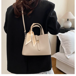 Détail du sac seau beige à texture litchi et foulard à motif cœur sur la poignée