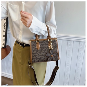 Detail of a brown monogram tote bag featuring a wide logo strap and a floral charm pendant