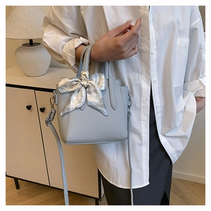 Détail du sac seau bleu clair à texture grainée avec nœud en soie et finitions argentées