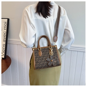 Detail of vintage brown tote bag with floral charm and jacquard strap shown on model