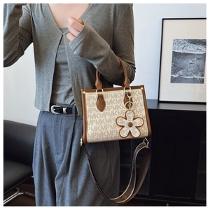 Detail of monogram tote bag featuring leather handles and floral charm accessory