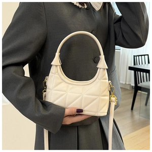 Detail of beige quilted hobo bag with gold hardware held by model in casual suit