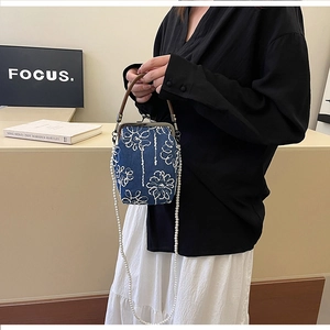 Détail de broderie sur sac en denim bleu avec bandoulière perle et anse cuir