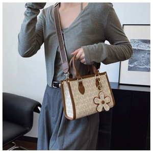 Detailed view of monogram tote bag with wide printed strap and floral charm accessory