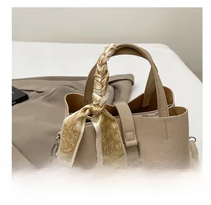 Détail d'un sac seau beige avec texture grainée et foulard en soie imprimé sur l'anse