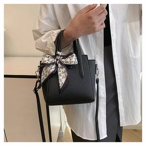 Détail d'un sac seau en cuir noir avec foulard en soie à cœurs et bandoulière amovible en métal