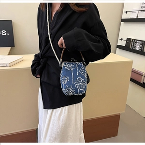 Détail du sac bandoulière en denim bleu avec broderie florale blanche et bandoulière perle