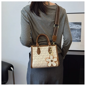 Detail of beige tote bag featuring letter print patterns and a floral charm accessory