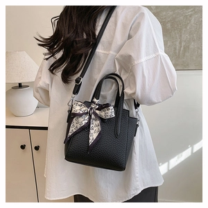 Détail d'un sac à main noir texture litchi avec foulard en soie à motif cœur sur la poignée