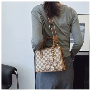 Classic patterned tote bag detail showing wide fabric shoulder strap and flower charm