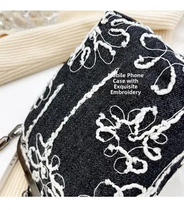 Détail de la broderie florale blanche sur le tissu en jean foncé du petit sac à bandoulière