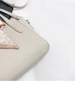 Détail d'un sac à main en cuir grainé beige avec foulard en soie à motif cœur sur l'anse