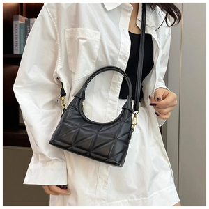 Detail of black quilted handbag with geometric triangle texture and gold hardware