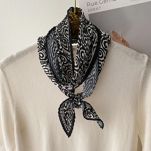 Pleated silk scarf with black and white geometric swirl pattern on white knitwear