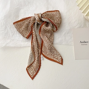 Detail of a pleated brown geometric silk scarf tied in a bow on textured paper