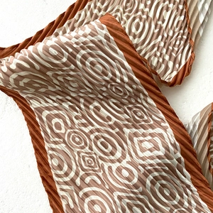 Detail of pleated silk scarf showing geometric concentric patterns and orange color blocking
