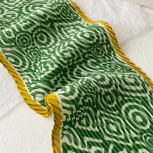 Detail view of green and white pleated silk scarf with yellow edges on white background