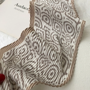 Close-up of pleated silk scarf with brown geometric spiral patterns on white fabric