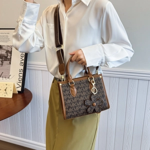Brown monogram tote bag with wide strap and floral charm shown in a modern interior