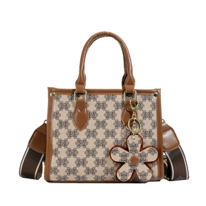 Brown monogram tote bag with top handles and adjustable floral charm strap in white background