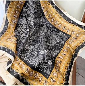Detail of silk satin scarf featuring elegant paisley patterns and golden border highlights