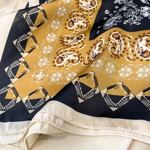 Detail of silk square scarf featuring gold paisley patterns and premium rolled edges