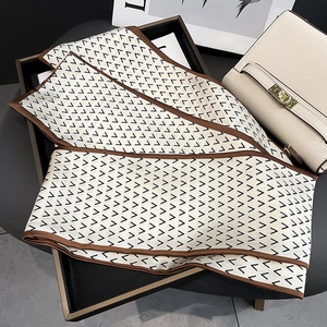 Detail of elegant letter printed silk scarf with geometric V-pattern folded in a tray