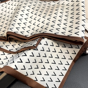 Detailed view of cream silk scarf with black geometric V pattern and brown borders