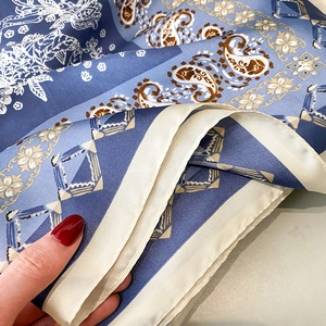 Macro detail of blue paisley silk scarf edge with professional stitching and hand texture