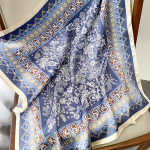 Detail of blue paisley floral silk scarf showing premium satin texture on a wooden chair