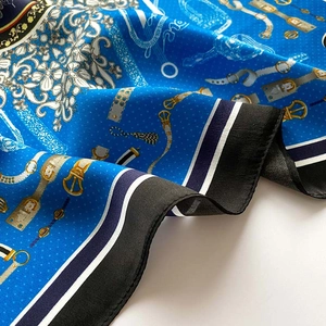 Gros plan sur un foulard en soie bleu roi aux motifs équestres et chaînes dorées