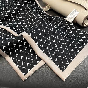 Detail of silk-feel scarf with V-pattern, elegant trim and fabric care label on leather bag