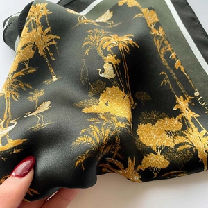 Detail of silk scarf featuring gold palm trees and crane prints on dark green fabric